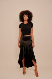 Fekete rövid felső és magas-alacsony szatén szoknya fodros részlettel. A szoknyán oldalsó hasíték található, amit arany színű, pántos magas sarkú cipő egészít ki.