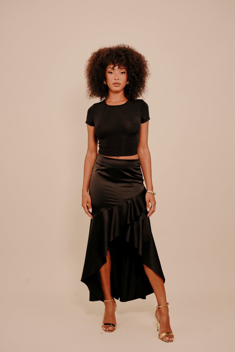 Fekete rövid felső és magas-alacsony szatén szoknya fodros részlettel. A szoknyán oldalsó hasíték található, amit arany színű, pántos magas sarkú cipő egészít ki.