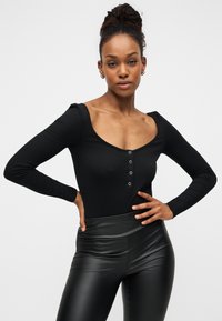 Μαύρο ριμπ κορμάκι με μακριά μανίκια, φαρδιά λαιμόκοψη και πατιλέτα με πέντε κουμπιά, συνδυασμένο με μαύρο κολάν από ψεύτικο δέρμα με ψηλή μέση.