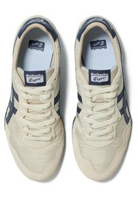 Sneakers beige con accenti blu navy, dotati di una tomaia testurizzata, chiusura con lacci e suole in gomma. Etichetta del marchio visibile sulla linguetta.