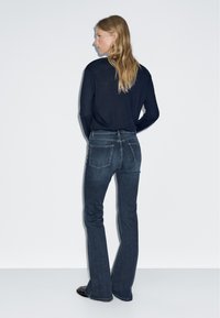 Tmavě modré zvonové džíny s vypasovaným pasem. Obsahují dvě zadní kapsy a minimální šití, doplněné černým topem s dlouhými rukávy.