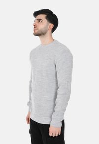 Maglione grigio chiaro a maglia con scollatura rotonda, polsini e orlo a coste. Presenta un design testurizzato e una silhouette aderente.