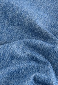 Tissu en denim bleu doux et texturé avec des fils subtilement plus clairs et plus foncés, montrant des plis et des froissements naturels.