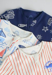 Trois bodies pour bébé avec boutons-pression à l'avant : un bleu marine avec des créatures marines, un blanc avec des bateaux et des poissons, et un blanc à rayures rouges avec un motif de poisson bleu.