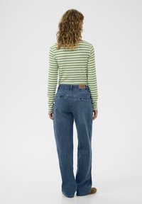 Prugasta zelena in bela majica z dolgimi rokavi, modri naravnost krojeni kavbojki in rjave obutve. Kavbojke imajo srednji pas in zadnji žep.