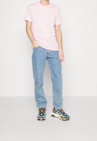 Light pink cotton t-shirt, relaxed fit, paired with blue denim jeans. Colorful patterned sneakers with varied textures and shades.