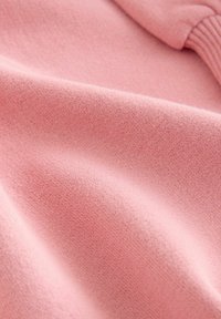Weiches, rosafarbenes Strickgewebe mit feiner Textur und gerippten Bündchen, die sanfte Falten und eine gemütliche Materialqualität zeigen.