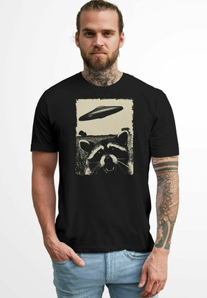 Black t-shirt featuring a vintage raccoon graphic with a UFO above, printed in black and beige tones, short sleeves, and crew neck style.