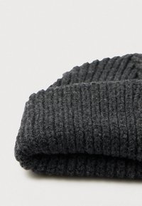 Tmavosivá rebrovaná pletená čiapka, zložená na ploche na svetlosivom pozadí.