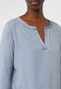 Lichtblau blouse van gladde stof, met een V-hals, lange mouwen en een subtiele glans. Eenvoudig ontwerp zonder zichtbare patronen.