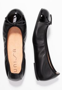 Mustat nahkaiset ballerinat, joissa on kiiltävä musta patenttikorko, nauhakoriste ja vaaleanruskea pohja. Mukana litteät kumipohjat mukavuutta varten.