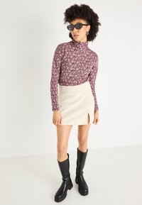 Top de cuello alto con mangas largas en color rosa con estampado floral, combinado con una falda crema de longitud a la rodilla que presenta una abertura lateral, y usado con botas negras hasta la rodilla.