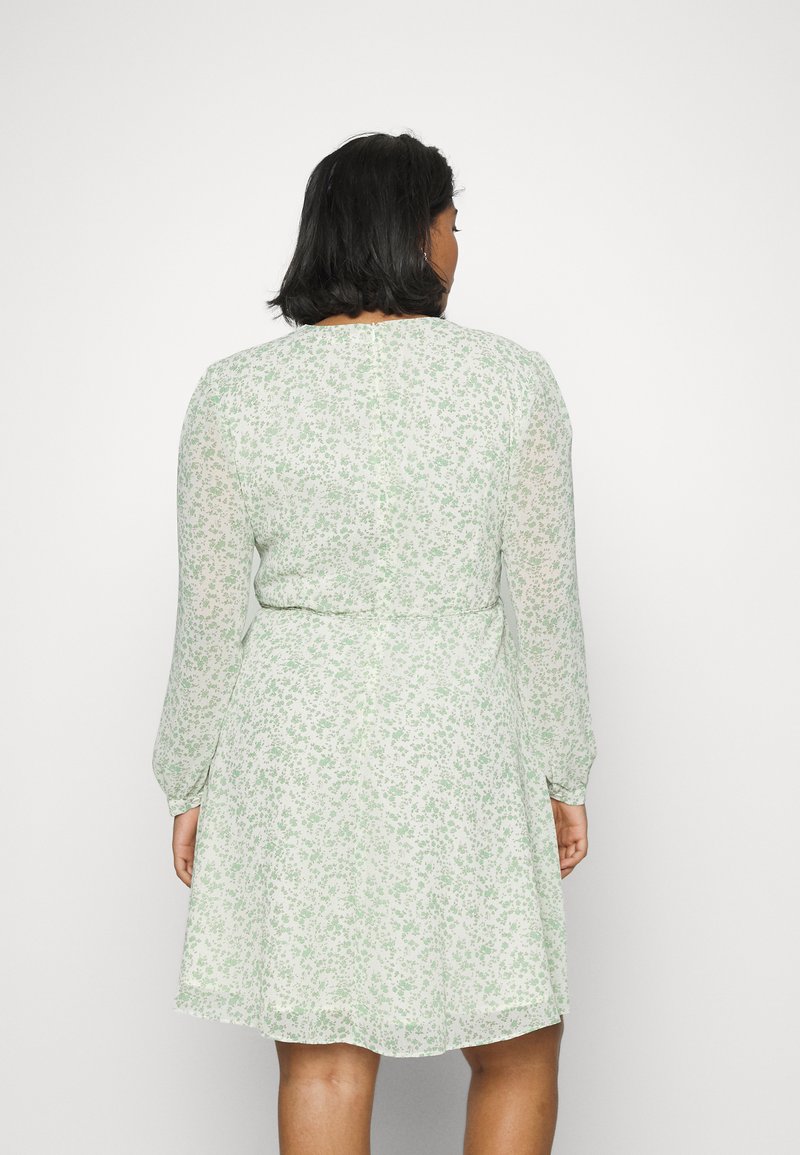 Vestido floral em tecido verde claro, com mangas longas, cintura ajustada e saia rodante. Pequenas flores brancas formam um padrão delicado.