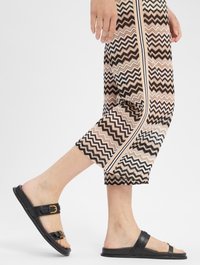 Czarne klapki z podwójnymi paskami i złotymi sprzączkami. Noszone z wzorzystymi, krótkimi spodniami z zygzakowatym wzorem w beżu i brązie.