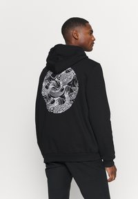 Black hoodie featuring a large, intricate white dragon graphic on the back. Made from soft fabric with a relaxed fit and a drawstring hood.