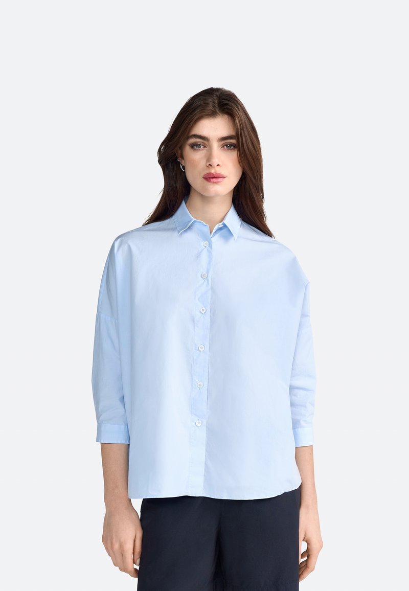 Light blue button-up shirt with a collar, three-quarter sleeves, and a relaxed fit. The fabric appears smooth and slightly shiny.