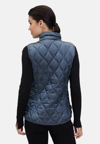 Gevoerde, marineblauwe vest met hoge kraag. Lichtgewicht stof met een ruitenpatroon; gecombineerd met een zwart hemd met lange mouwen eronder.