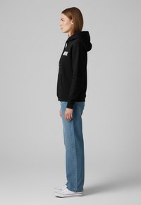 Felpa nera con logo bianco, tasca a marsupio, polsini a costine, abbinata a jeans azzurri a gamba dritta e sneakers bianche.