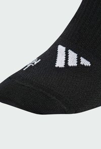 Media deportiva negra con tejido texturizado, cuenta con un logo blanco y un diseño a rayas. Punta redondeada y detalle de talón reforzado.