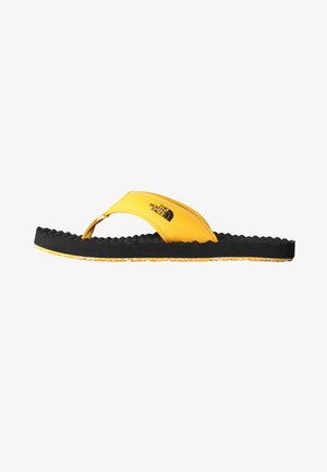 Keltainen flip-flop mustalla tekstuurilla varustetulla pohjalla ja nylonhihnalla, jossa on logo. Muotoilu sisältää urheilullisen, rentoa siluettia kontrastiväreillä.