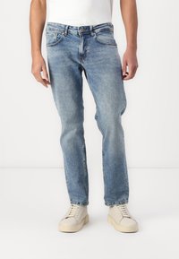 Helle blaue Denim-Jeans mit geradem Schnitt, fünf Taschen und Kontrastnähten, kombiniert mit weißen Sneakern.