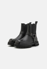 Stivali alla caviglia in pelle nera con pannelli laterali elastici, punta arrotondata e suola in gomma chunky; presentano un accento metallico circolare e dettagli con cinturino.