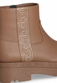Bottino marrone realizzato in materiale sintetico liscio, caratterizzato da un accento con logo silver e suola in gomma testurizzata con dettagli del marchio.
