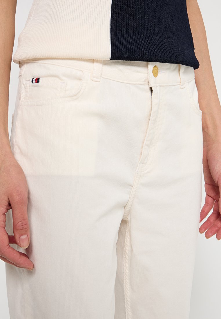 Białe bawełniane spodnie o teksturowanym wykończeniu, z złotym guzikiem, kieszeniami z przodu i małym, wielokolorowym logo na lewej kieszeni.