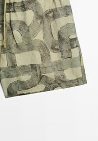 Baumwollshorts mit einem grauen abstrakten Pinselstrichmuster auf einem hellbeigen Hintergrund, mit einem Kordelzug und genähten Saumdetails.
