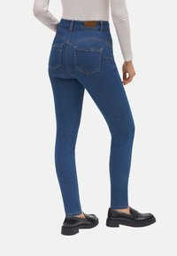 Jeans de mezclilla azul ajustados con una cintura alta, bolsillos traseros y detalles de costura visibles. Lucen con mocasines negros.