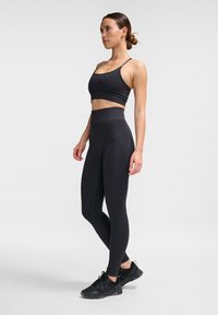 Svart träningsklädsel med en åtsittande crop top och högmidjade leggings, båda gjorda av mjukt, stretchigt material. Åtföljd av svarta sneakers.