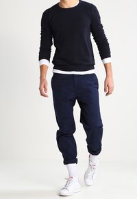 Granatowy sweter prążkowany z białymi mankietami, połączony z granatowymi spodniami o zwężanym kroju. Białe sneakersy i skarpetki za kostkę dopełniają stylizację.