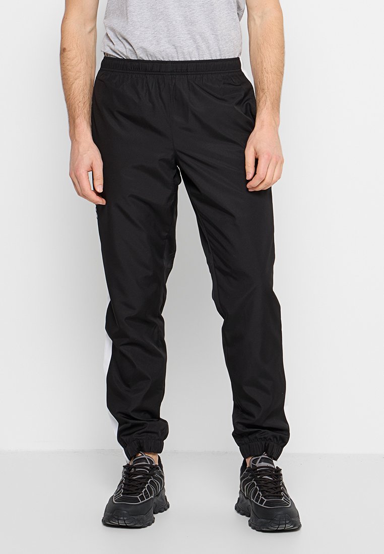 Pantalons de sport noirs avec une taille élastique et des poignets de cheville, présentant des rayures blanches sur le côté pour le contraste. Le matériau semble léger et lisse.