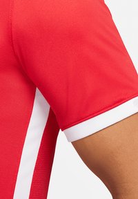 Rotes Sporttrikot aus strukturiertem Stoff, mit kurzen Ärmeln und weißen Seitenstreifen, sowie einem gerippten weißen Kragen.