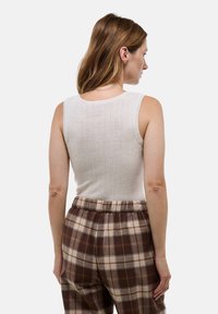 Débardeur crème à côtes avec un col rond, associé à un pantalon à carreaux ample dans des tons marron et beige.