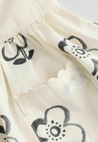 Weißer Stoff mit schwarzem Blumenmuster; gerafftes Oberteil mit gewelltem Saum und genähten Taschendetails. Leichtes, strukturiertes Material.