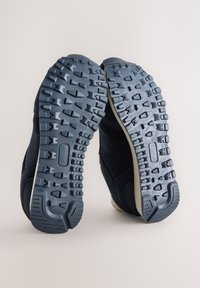 Chaussures de sport bleu marine avec semelles en caoutchouc texturées. Les semelles présentent des crampons proéminents pour une meilleure adhérence, et la tige est composée d'un tissu sombre et doux.