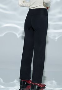 Pantalon large noir côtelé avec une taille haute, associé à des chaussures à talons rouges. Texture lisse, lignes verticales qui mettent en valeur le design.
