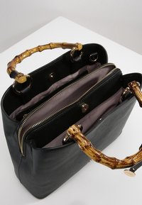 Černá kožená kabelka s úchyty ve stylu bambusu, otevřená nahoře s viditelnými vnitřními přihrádkami se zipem a s překlopným uzávěrem, s béžovým podšívkou.