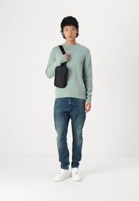 Suéter de malha verde-claro, jeans azuis e ténis brancos. Uma pequena bolsa preta a tiracolo é usada no ombro. Conjunto simples e casual.