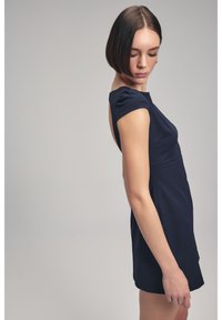 Vestido ajustado de color azul marino con mangas cortas, diseño de espalda descubierta y textura suave. Presenta un corpete estructurado y una longitud corta.