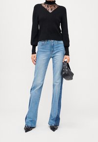 Maglione nero in maglia con inserto in pizzo, jeans azzurri svasati, tacchi neri appuntiti e una piccola borsa nera con dettagli in occhiello.