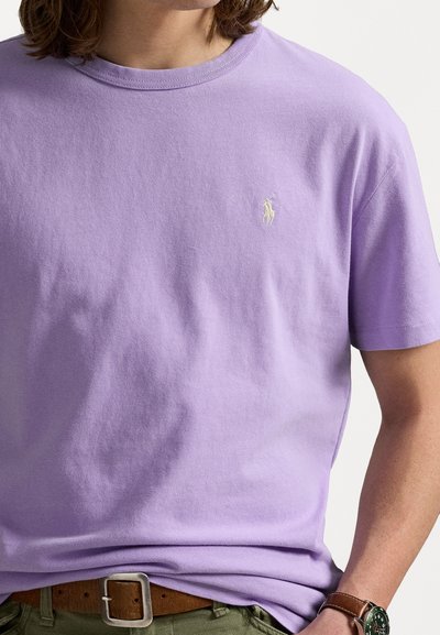 Lila bomull t-shirt med rund halsringning, korta ärmar och en liten broderad logotyp på vänster bröst. Har en avslappnad passform.