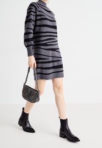 Grijze trui-jurk met zwarte zebraprinten, geribbelde manchetten en halslijn. Accessoires omvatten een zwart handtas met structuur en zwarte enkellaarsjes.