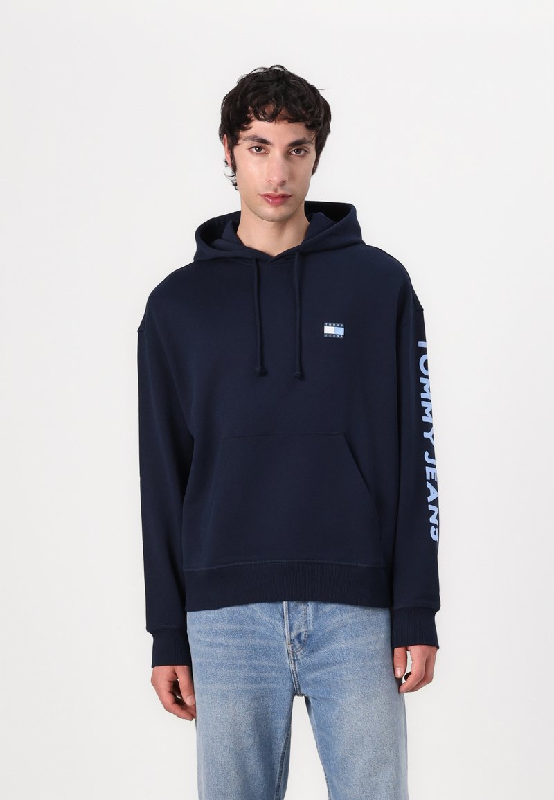 Sudadera de marina hecha de un tejido suave, con un bolsillo canguro frontal, capucha con cordón y logotipo "TOMMY JEANS" en blanco en la manga.