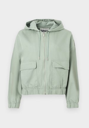 Svetlo zelena kratka jopa s kapuco, sprednjo zadrgo, dvema žepoma s poklopcem, kapuco z vrvico ter elastičnimi manšetami in spodnjim robom.