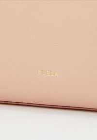 Světle růžová kožená taška s texturovaným povrchem, zdobená zlatým embosovaným logem "Furla". Ozdobená tmavším růžovým lemem.