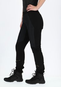 Zwarte outdoorbroek met een slim fit, hoge taille, waterafstotend materiaal en ritszakken aan de zijkant, gecombineerd met zwarte wandelschoenen.