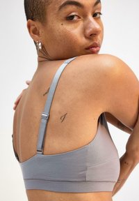 Grå, blød stofbralette med justerbare stropper, der har et stilrent design. Glat tekstur og minimalistisk stil med lette elastiske detaljer.