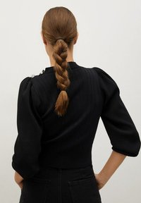 Pull noir côtelé à manches trois-quarts bouffantes, avec des accents décoratifs sur l'épaule et une ceinture ajustée.